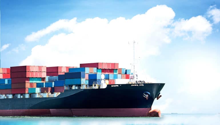 A large container ship sits on a glassy ocean under a large white cloud