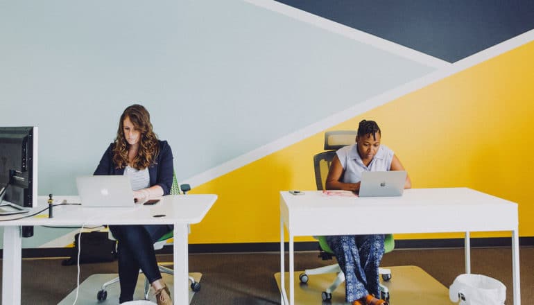 two serious people at small desks in office