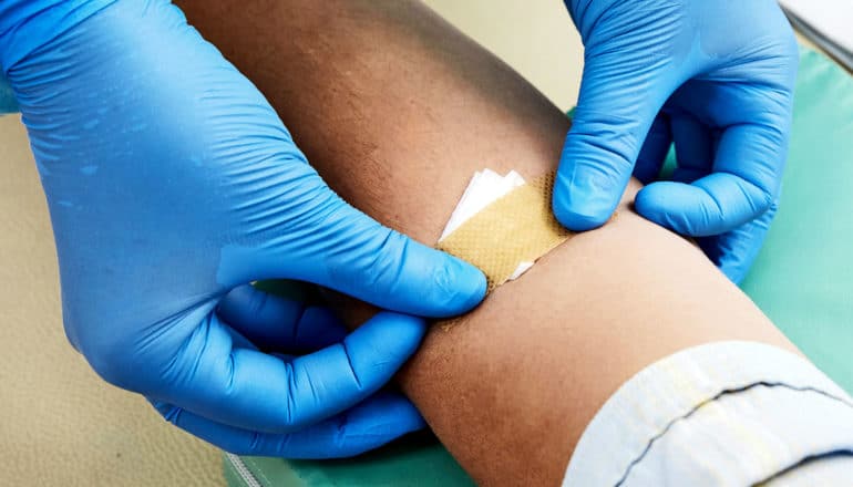 A health care worker wearing blue gloves puts a bandaid over a patient's blood test site.