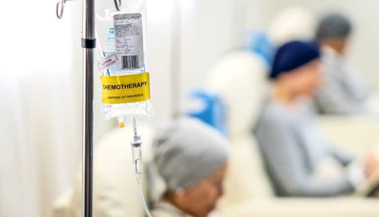 A hanging IV bag stands next to patients receiving chemotherapy.