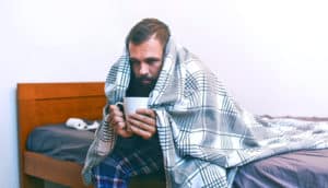 person holding mug sits on bed under blanket