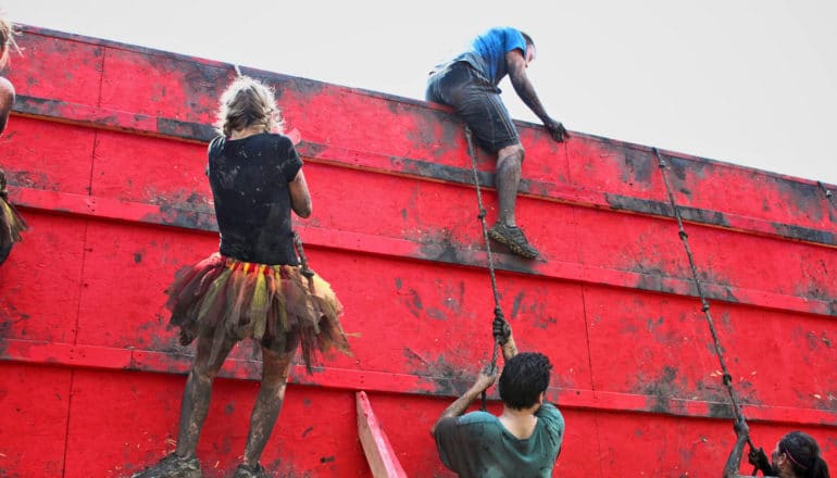 people scale wall during tough mudder