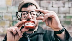 man holds up glasses and toy teeth