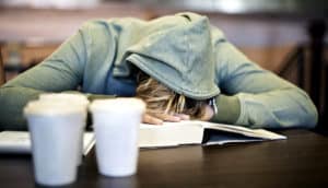 student sleeping on books on library desk