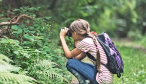 girl with backpack uses binoculars