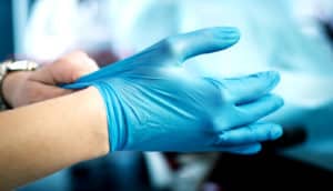 health care worker pulls on blue glove