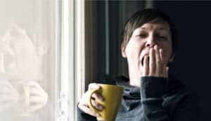 woman yawns and holds yellow mug