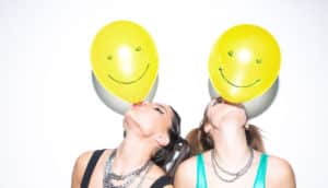 two women blow up yellow smiley balloons