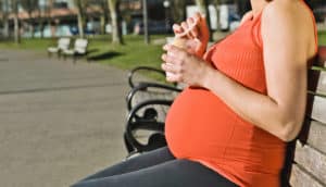 pregnant woman in red eats yogurt on bench