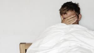 man covers face in bed
