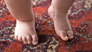 bare feet of baby learning to walk on rug
