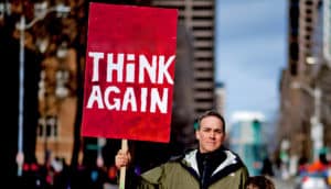 man holds red "think again" sign