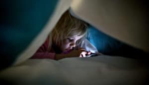 girl under covers with phone (sneaky media use)