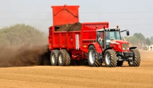 red tractor sprays manure on field - antibiotics in manure