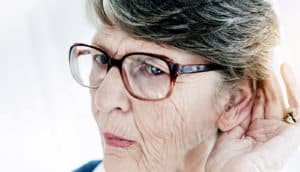 older woman holds hand behind ear - cost of hearing aids