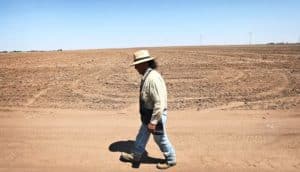 man walking by barren field (extreme weather concept)