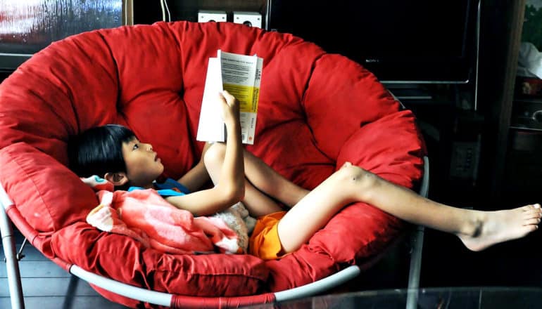 kid reading in red chair (dyslexia concept)