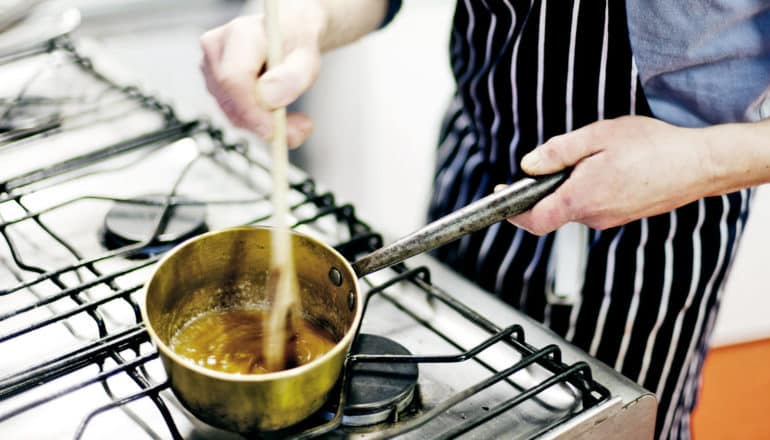 person stirs caramel sauce in pot on stove