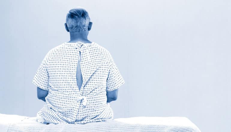 man in gown sits on hospital bed facing away