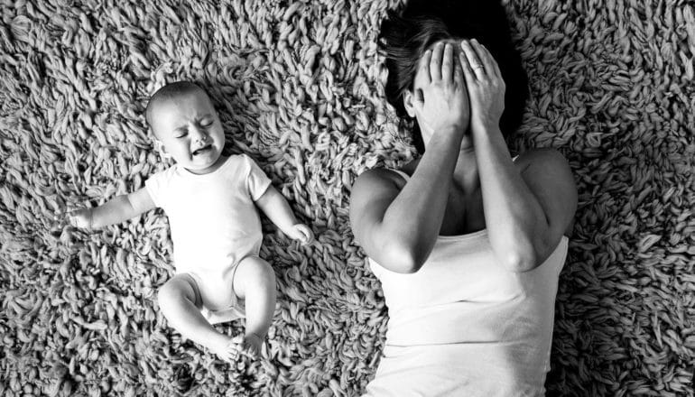 crying baby and mom covering face on carpet