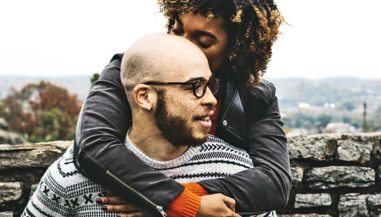 woman kisses man's head by stone wall