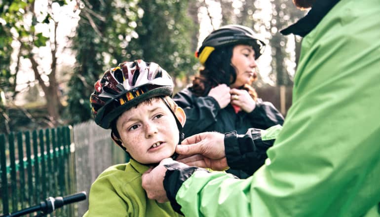 hands buckle kid's bike helmet, woman in background