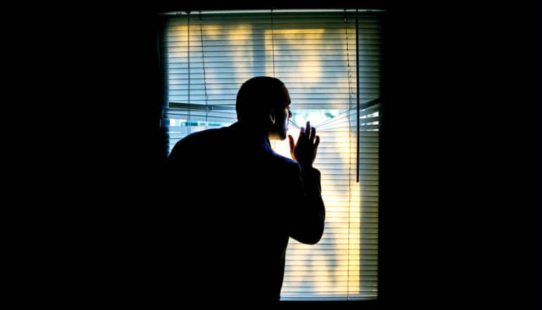 man looking through blinds (mindfulness concept)