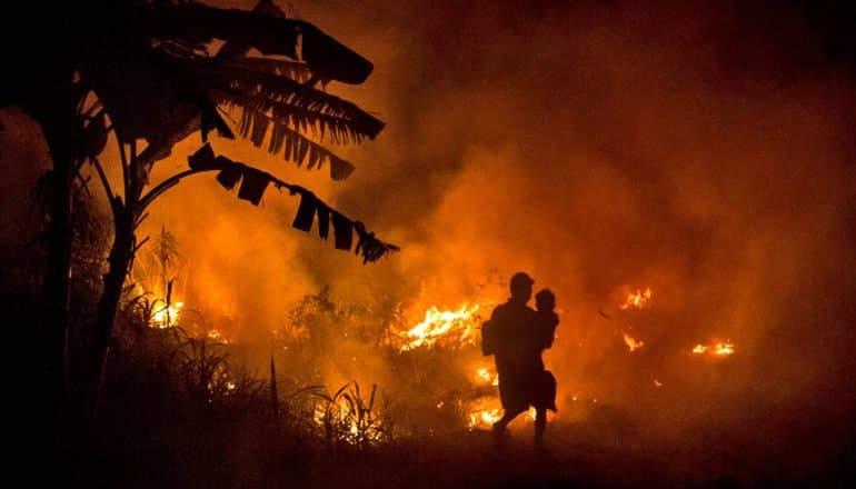 silhouetted man carries child past fire in Indonesia