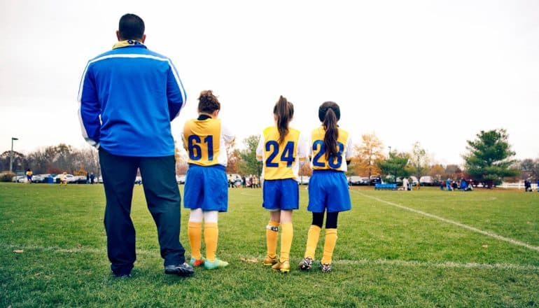 coach and three girls on edge of soccer field