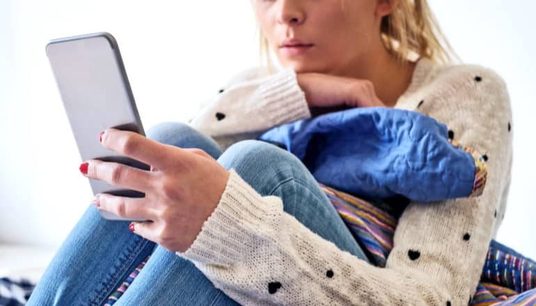 young woman using phone curled up (depression concept)