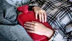 hands on red hot water bottle on abdomen