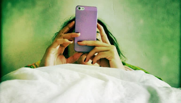 person uses phone in bed against green wall