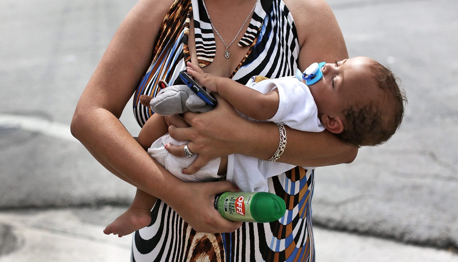 woman holds infant and can of bug spray