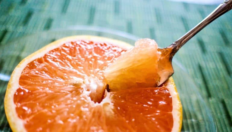 spoon in pink grapefruit on green surface