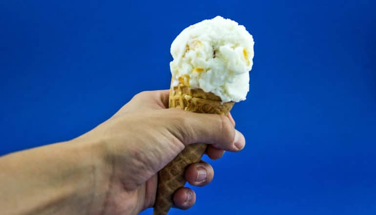 hand holds ice cream cone against blue background