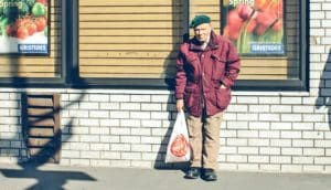 older man in winter coat standing outside grocery store