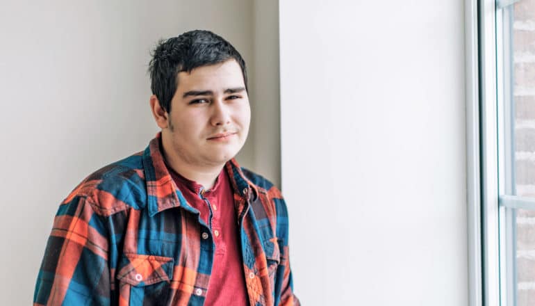 skeptical teen guy in plaid by window