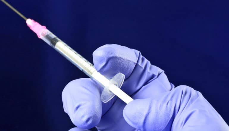 purple gloved hand with syringe