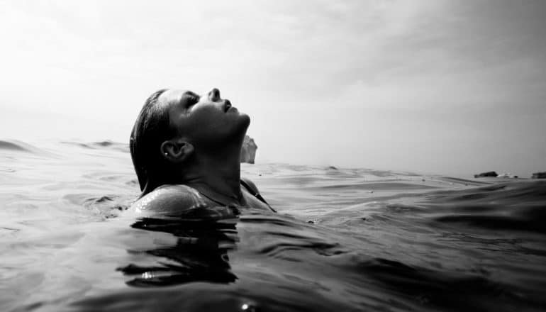 b/w image of woman surfacing from under ocean water