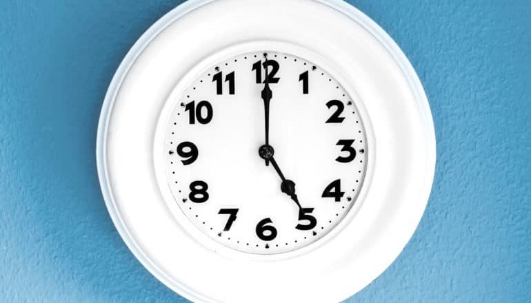 white clock says 5 o/clock on blue wall