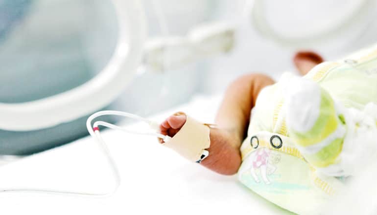 foot of newborn baby in incubator with pulse oximeter