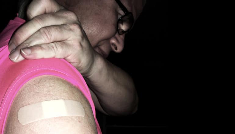 person pulls up pink sleeve to show bandaid from vaccination