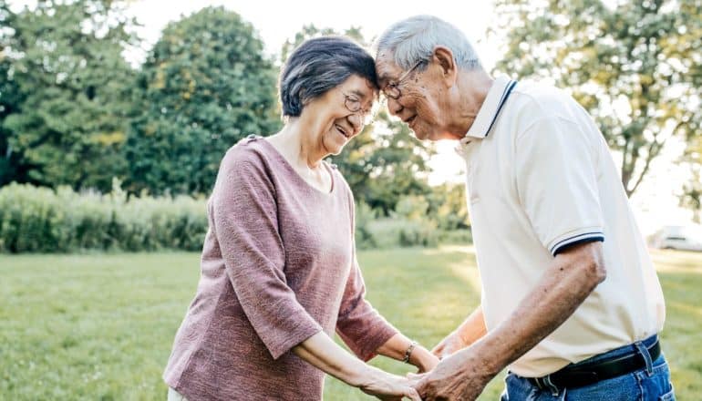 elderly woman and man touch foreheads outdoors