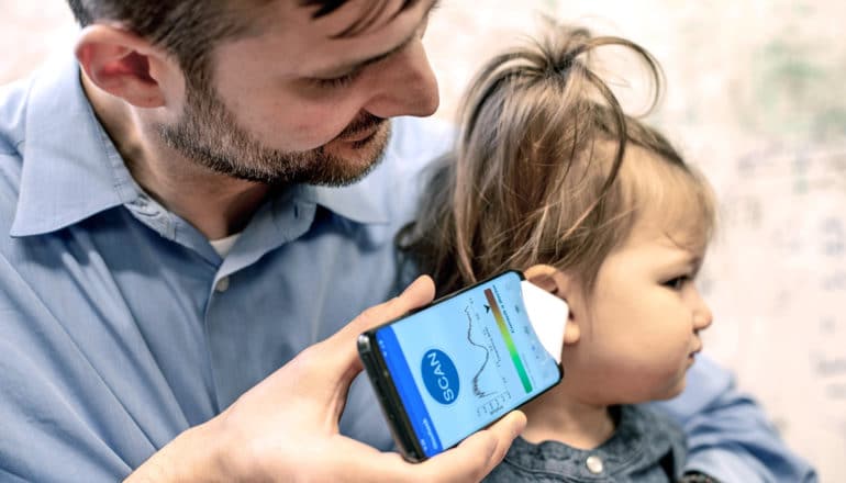 father holds ear infection app on phone to daughter's ear