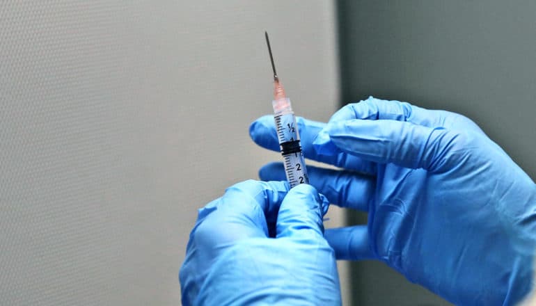 ebola vaccine syringe in blue-gloved hands