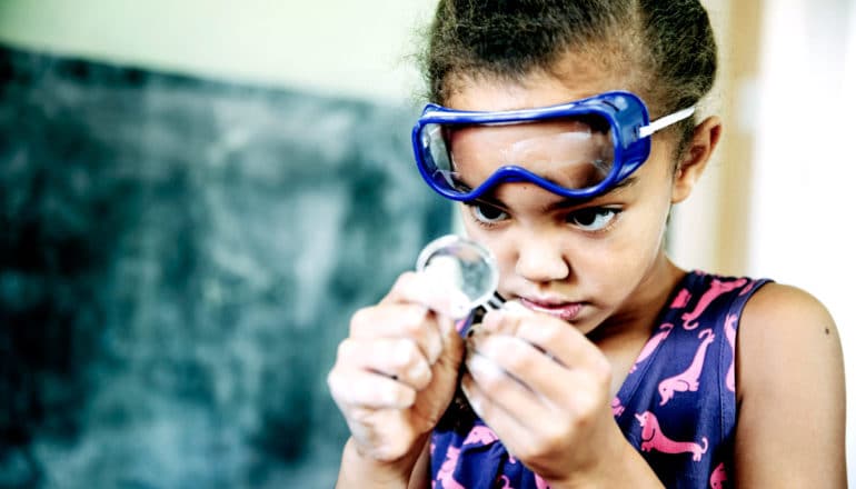 girl in goggles uses magnifying glass