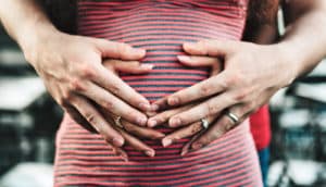 parents' hands on pregnant belly in striped top