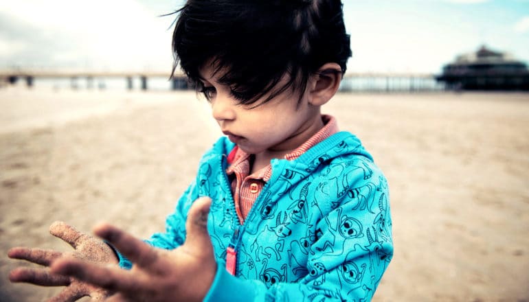 child on beach looks at sandy hands - motor deficit