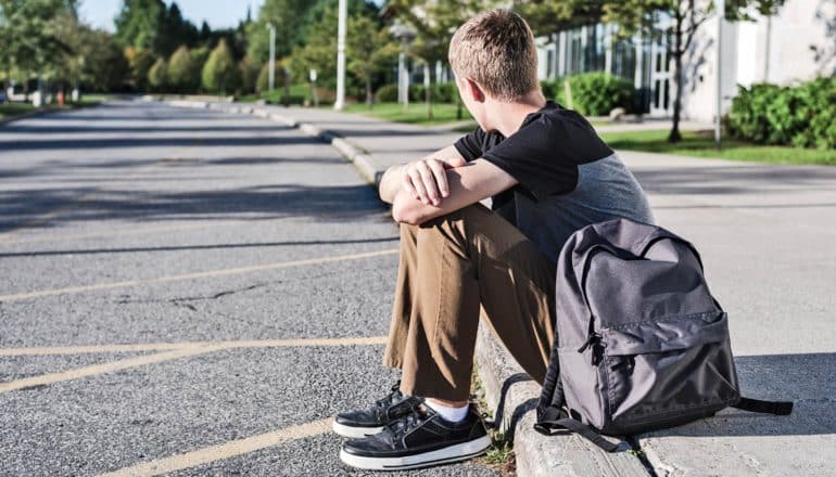 masculinity - teen guy with backpack on curb