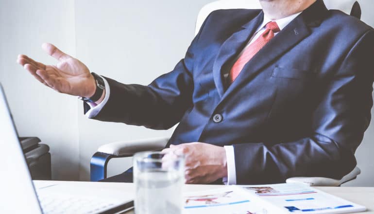 man in suit at desk gestures